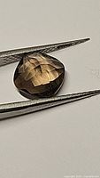 Close-up image showing cushion checkerboard cut smokey quartz held by tweezers, highlighting the gemstone's clarity and cut facets.