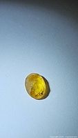 Photo of bright yellow natural fancy oval rose cut sapphire on a plain background showing gemstone shape, cut, color and clarity.