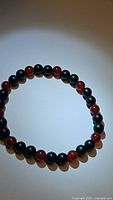 Top-down photo of a stretchy bracelet with alternating black onyx and red carnelian beads laid flat in a circle on white surface