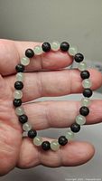 Photo showing the stretchy bracelet held in hand, beads alternating between black lava and green aventurine.