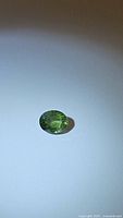 Top-down view of the oval cut green sapphire gemstone on a white background showing clarity and color.