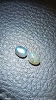 Two oval cabochon labradorite gemstones showing blue flash on a textured black surface.