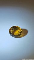 Oval faceted natural Madeira citrine gemstone pictured on a flat surface under lighting to show color and clarity.