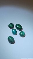 Five oval natural malachite stones displaying range of green banded patterns with smooth polished surfaces.