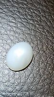 Oval white cabochon cut natural moonstone gemstone with a polished surface and visible adularescence.