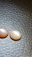 Photo shows two polished oval moonstone cabochons on black textured background, one peach purple and one milky light color.