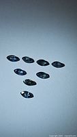 View of 9 marquis cut natural multicolored sapphires showing blue and green hues scattered on a surface.