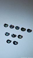 Eleven loose round faceted multicolored sapphires placed on a white background, showing color variety mainly in green, yellow, and blue hues