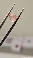 Close-up image of the natural peach sapphire held by tweezers, showing the pear checkerboard cut and translucent peach color.