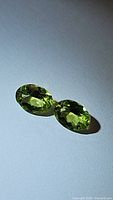 Two natural oval cut peridot gemstones showing apple green color and facets reflecting light, matching pair.