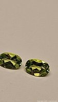 Close-up photo of two oval cut apple green peridot gemstones showing their color and faceting