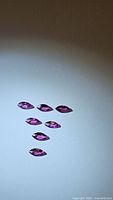 Seven marquis cut pink purple Rhodolite garnet stones laid out on white background with good light.