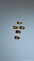 Five natural baguette cut sapphires in shades of yellow and orange displayed on a gray surface.