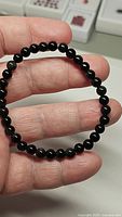 Stretchy natural jet black rainbow obsidian bead bracelet held on hand, showing round glossy beads and elastic cord.