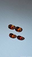 Four loose oval faceted deep fire orange Imperial sapphire gemstones arranged on white background