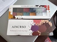 Top view of the 12 color face paint palette in white cardboard box with transparent window showing multiple paint colors.