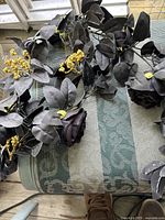 Image of artificial Halloween-themed floral garland featuring black fabric flowers, dark leaves, and yellow berry accents laid out on a fabric surface.
