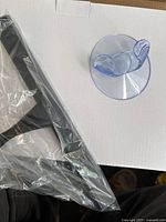 Photo showing the stainless steel squeegee partially covered in plastic packaging and a clear plastic suction hook.