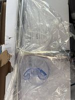 Photo showing stainless steel squeegee and transparent suction hook in clear plastic wrappers resting on cardboard surface.