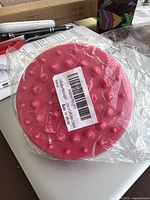 Close-up of the pink base of the cellulite massager showing raised rounded and pointed nodes for massage purposes, still wrapped in clear plastic packaging.