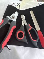 Clear photo showing three pet grooming tools including nail clippers, nail scissors, and nail file along with a black drawstring pouch, highlighting the black and red color scheme and tool details.