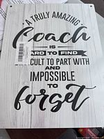 Front of wooden wall hanging with the motivational quote about a coach, printed in black on light woodgrain background.