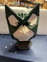 Front view of green and white resin decorative owl figurine showing geometric origami-inspired design and facial features.