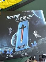 Packaging of the Magic John tempered glass screen protector with space and astronaut graphics, showing product features: scratch resistant, easy installation, drop resistant.