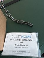 Close-up of matte graphite metal chain link and installation instructions for chain tiebacks from Blast Home Signature Collection.
