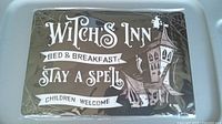 Front view of the metal Witch's Inn sign in plastic wrap showing the Halloween themed design and text.