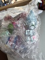 Photo showing multicolored plastic figurines sealed in clear plastic bag with various shapes visible including humanoid and fantasy designs.