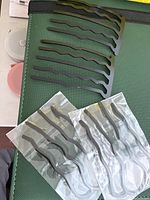 Individual black metal hair combs arranged on a surface alongside two sealed packs each containing multiple combs.