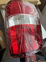 Front view of red and clear lens tail light housing wrapped in plastic.