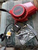 Top view photo of all components including red recoil starter, spark plug, fuel filter, hoses, and tools arranged on a surface.