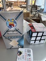 Sengso Legend 3-layer magic cube in open foil packaging alongside its box and instruction manual on table.
