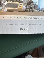 Box label showing Luna By Camilla brand, product details including 12-inch taper candles, quantity of 10 pieces, 9-hour burn time, and rose scent.