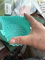 Hand holding a turquoise silicone bowl with scalloped edges and ribbed swirl pattern base, showing size and grip texture.