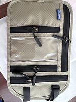 Front side of multifunctional halter showing beige fabric material with several black zipper compartments, including transparent pocket.