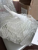 White sea glass pieces contained in a white mesh drawstring bag on a surface with a cardboard box in the background.