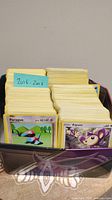 Photo showing multiple stacks of Pokemon cards in a box with a note indicating years 2016 to 2018, cards include Porygon and Aipom visible in front.