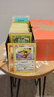 Photo of a collection of Pokemon cards including visible cards marked Beedrill and Pidgeot, stored in a box with dividers labeled 2019