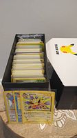 Photo of a black storage box filled with neatly stacked Pokemon trading cards showing yellow borders and partial card fronts including Jolteon card.