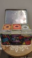 Photo showing a colorful metal storage tin filled with multiple stacks of Pokemon cards. Visible energy cards on top include Fire, Fighting, and Steel type cards.