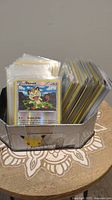 Photo of a collection of Pokemon cards in plastic sleeves stored upright in a metal holder with Pikachu decal on front.