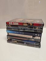 Stack of 10 DVDs showing titles on the spines including Red Dawn, Missing, The Last Sign, Dementia 13, Astro, Taken, Unbelievable, Motherhood, Seabiscuit and The Canterville Ghost