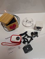 Photo showing Love Box with red heart design, wireless charging pad, WYZE camera cube, Polaroid action camera with mounts and user manual