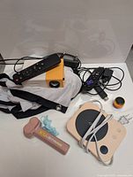 Showcasing the projector unit with remote, cables, and KU-STRING flow toy with blue string, mug warmer, and mini Bluetooth speaker on a white surface.