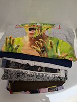 Stack of 8 folded graphic t-shirts showing upper green slime creature graphic shirt on top