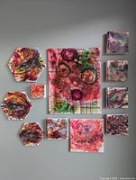 Photo showing all 11 paintings arranged on a gray wall revealing the size, shape, and abstract red-themed designs.