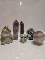 Front view of all six large semi-precious gemstone carvings arranged in a line on a reflective white surface showing their polished surfaces and natural patterns.